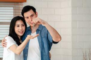 Happy smiling couple in front of the home and holding keys to New Home On Moving In Day, and start a new life family. Concept of homeowner and relocation photo