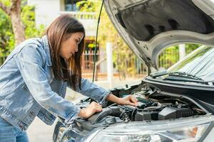 Angry Asian woman and using mobile phone calling for assistance after a car breakdown on street. Concept of vehicle engine problem or accident and emergency help from Professional mechanic photo