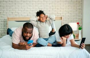 las niñas afroamericanas no están satisfechas y tristes, sentadas en medio entre padre y madre. los padres están usando el teléfono inteligente y los niños abandonados. los niños necesitan la atención de sus padres. foto