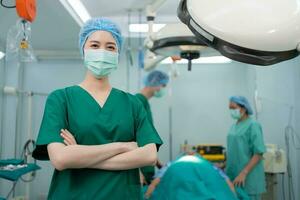 retrato de asiático cirujano y enfermero con médico máscara en pie con brazos cruzado en operación teatro a un hospital. equipo de profesional cirujanos cuidado de la salud, emergencia médico Servicio concepto foto