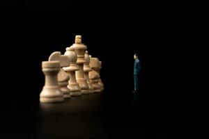 Figures businessman standing in front of wooden chess on black isolated background. Concept of business analysis and strategy. Stepping into the startup, new business player photo