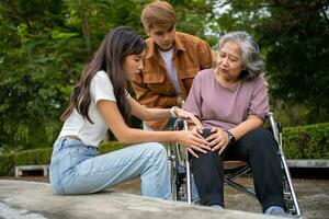 Asian careful caregiver or nurse taking care of the patient is hurting knee in wheelchair. Concept of happy retirement with care from caregiver and Savings and senior health insurance, a Happy family photo