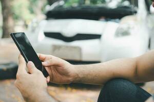 Asian man using smartphone for assistance after a car breakdown on street. Concept of vehicle engine problem or accident and emergency help from Professional mechanic photo