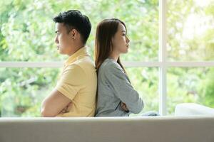 Unhappy Couple sitting behind each other on the couch and avoid talking or looking at each other, Cause of relationship problems and having misunderstanding or disagreement. Family problems concept photo