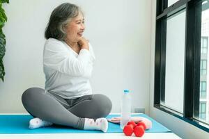 Senior Asian woman watching online courses on a laptop while exercising in the living room at home. Concept of workout training online. photo