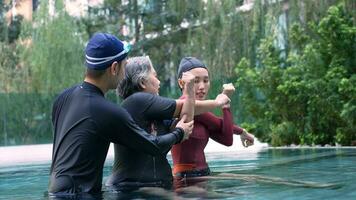 Young trainer helping senior woman in aqua aerobics and working out in the pool. old woman and mature man doing aqua aerobics exercise in swimming pool, Elderly sports, and active lifestyle concept. photo