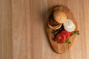 Top view of fresh tasty homemade hamburger with fresh vegetables, lettuce, tomato, cheese beside sliced tomatoes on a cutting board. Free space for text photo