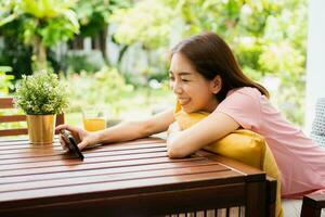 Happy Asian woman sitting in the backyard and holding smartphone for watching a movie series during relax time. photo