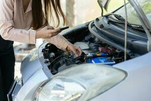 Angry Asian woman using a smartphone VIDEO conference for assistance after a car breakdown on street. Concept of a vehicle engine problem or accident and emergency help from a Professional mechanic photo