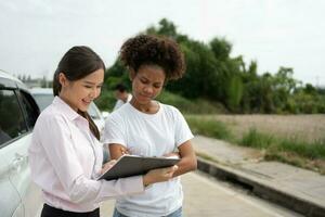 Women drivers Talk to Insurance Agent for examining damaged car and customer checks on the report claim form after an accident. Concept of insurance, advice auto repair shop and car traffic accidents. photo