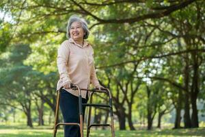 Happy old elderly Asian woman uses a walker for osteoarthritis rehabilitation physiotherapy in park.  Concept of happy retirement With care from a caregiver and Savings and senior health insurance photo