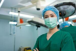 Portrait of Asian surgeon and nurse with medical mask standing with arms crossed in operation theater at a hospital. Team of Professional surgeons. Healthcare, emergency medical service concept photo