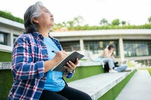 Mature adult student sitting in front off College building and reading school books after attending a university class, Adult education Learning Studying Happy Asian Elderly retired activity photo