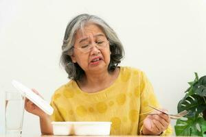 Unhappy Asian senior woman anorexia and say no to ready meals, Elderly home alone and bored food and no appetite photo