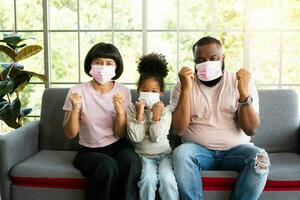 Mixed Race family sitting on the sofa and wearing medical face masks for against coronavirus world pandemic and stay quarantined together at home social distancing new normal lifestyle photo