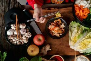 asiático mujer vistiendo coreano tradicional disfraces hanbok son mezcla Fresco Salteado y kimchi ingredientes con ingredientes tal como sal, ajo, gochugaru, Fresco vegetales. foto