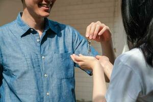 Happy smiling couple in front of the home and holding keys to New Home On Moving In Day, and start a new life family. Concept of homeowner and relocation photo