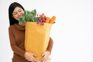 Happy Asian woman is smiling and carries a shopping paper bag after the courier from the grocery came to deliver his goods at home. Concept of Supermarket delivery for a new lifestyle photo