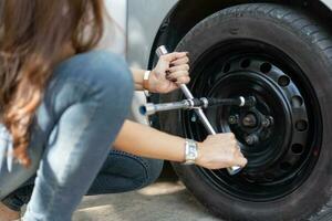 Smart and Attractive Asian woman jacks up her car and uses a wrench to change the wheel on a broken car, uses tools or equipment, tries to solve problems by self, Car Repairing and insurance concept photo