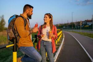 adulto Pareja descansando junto a el la carretera y Bebiendo refresco jugo. foto