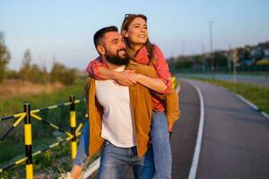 Happy smiling couple enjoying sunset. Man is carrying on back his woman. photo