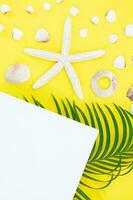 blanco estrella de mar, conchas con palma hojas y papel para texto en lado en amarillo antecedentes. plano poner. viajar, vacaciones, verano. Copiar espacio foto