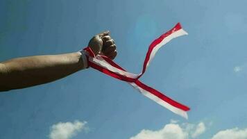 Hand with red and white ribbon with blue sky background, Indonesia independence day celebration concept video