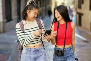 alegre asiático viajeros utilizando Teléfono móvil mientras caminando en urbano calle foto