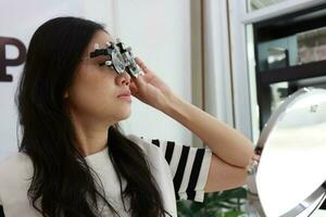 tailandés dama vistiendo los anteojos dentro el clínica, mujer en óptico foto