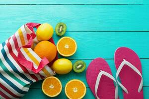 Summer fun time and fruits on blue wooden background. Mock up and picturesque. Orange, lemon, kiwi fruit in bag and flip flops on the floor. Top view and copy space photo