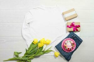 Closeup white blank template sweatshirt hoodie copy space. Mothers women day yellow tulips, gifts. Happy birthday top view mockup pullover. White wooden background. Casual outfit. Flat lay templates photo