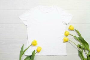 blanco camiseta Bosquejo. modelo blanco camisa parte superior vista. blanco de madera antecedentes. madre mujer día día festivo. amarillo tulipanes mujer camiseta con cumpleaños ramo de flores flores primavera mirar. hembra accesorios foto