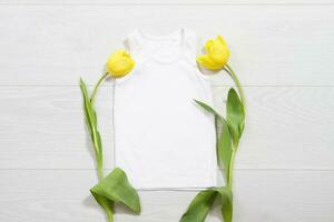 White children t-shirt mockup. Template blank kids shirt top view. White wooden background. Mother women day holiday. Yellow tulip. Baby tshirt with birthday flower. Spring look. photo