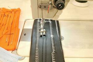 Close-up of sewing machine working with with thread inserted on the needle and fabric item of clothing. Workplace of seamstress. Sewing process in the phase of overstitching photo