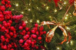 Close-up of Christmas tree in the house with decoration. Garland, lights, rowanberries and flowers on spruce fir branches. Winter holidays composition photo
