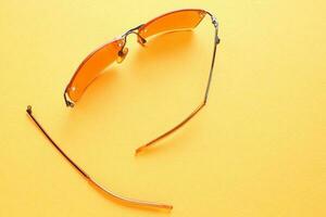 Old broken eyeglasses with damaged legs on yellow background. Poor eyesight. Reuse and repair concept. Idea of health. Failure optic eyewear. Breakage of vision correction glasses. Close up, flat lay photo