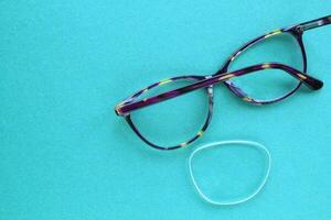 Old broken eyeglasses with damaged lens on blue background. Poor eyesight. Reuse and repair concept. Idea of health. Failure optic eyewear. Breakage of vision correction glasses. Close up, flat lay photo