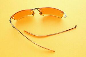 Old broken eyeglasses with damaged legs on yellow background. Poor eyesight. Reuse and repair concept. Idea of health. Failure optic eyewear. Breakage of vision correction glasses. Close up, flat lay photo