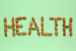 almendra nueces arreglando en a un palabra salud en verde antecedentes. sano comiendo, crudo comida dieta, nutrición, vegetariano concepto. proteína orgánico seco bocadillo, cereales. nacional nuez día. Copiar espacio para texto foto