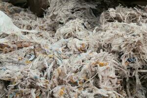 Shredded plastic pieces prepare for recycling. Raw cables material for reproduction. Sorting garbage on waste plant. Pile of scrap bottles on trash storage factory. Environmental concept photo