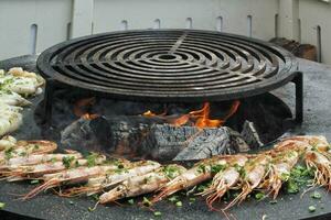 Seafood slices are cooked on a fire pit surface in the shape of cone shaped bowl. Bowl-shaped flat grill with prawns and shrimps. Outdoor barbecue cooking. Street food concept. Toast the hot grilled photo
