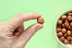 mujer participación orgánico avellana en su mano en verde antecedentes. nutrición sano comida elección concepto. calorías dieta bocadillo. sostenible estilo de vida. de cerca foto