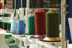 Close-up of spools of color threads, spinning machine. Yarn bobbins making in a textile factory. Embroidery machine in garment industry. Dyeing fabrics yarn. Sewing material tool photo