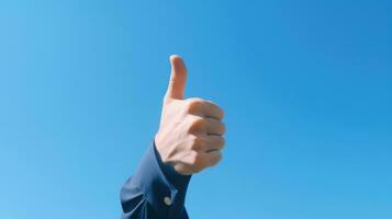 an adult hand giving a thumbs-up gesture against a clear, blue sky. The hand appears isolated, with no other objects or people in the frame. It's a simple yet cheerful scene photo