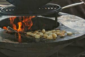 Seafood slices are cooked on a fire pit surface in the shape of cone shaped bowl. Bowl-shaped flat grill with scallop and octopus. Outdoor barbecue cooking. Street food concept. Toast the hot grilled photo