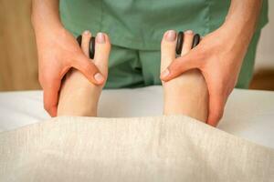 Massager doing feet and toes massage with rocks between a female toes. photo