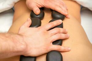 Young caucasian woman receiving back massage with black stones by masseur in spa salon. A woman getting a spa treatment. photo