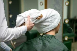 A hairdresser is wrapping the wet hair of the young woman in a towel after washing at the beauty salon. photo