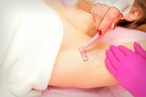 Beautician shaves the armpit of a young woman with a razor before the hair removal procedure. photo