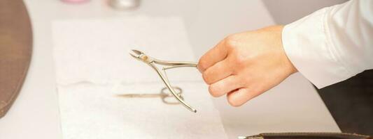 Nail nippers in the hand of female manicure master putting to the towel before nail care in manicure salon. photo